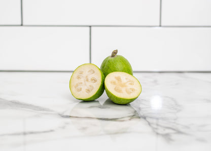 Feijoa fruit, cut in half on a marble surface with a tiled wall background.
