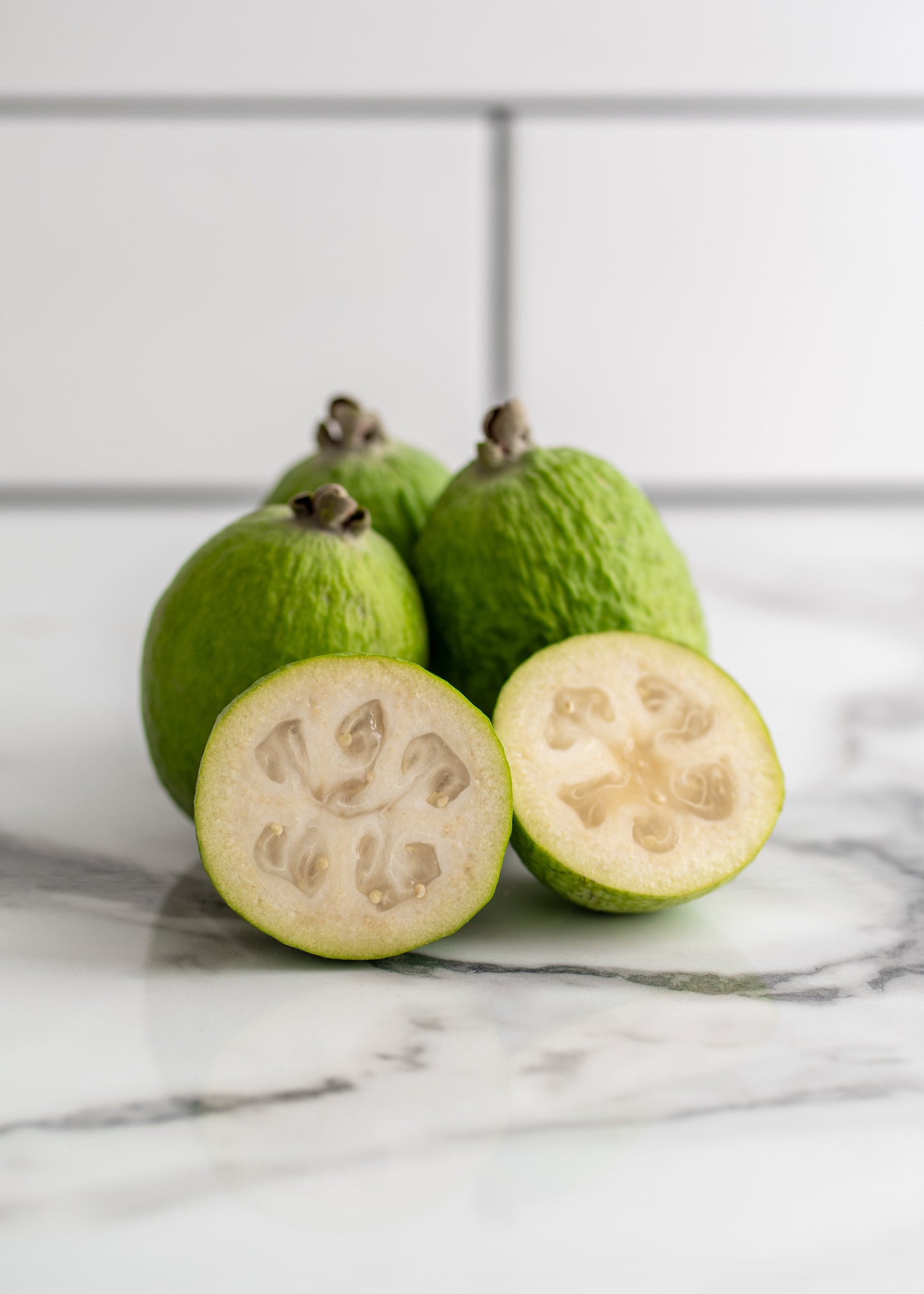 Feijoa fruit with a sliced feijoa on a marble surface