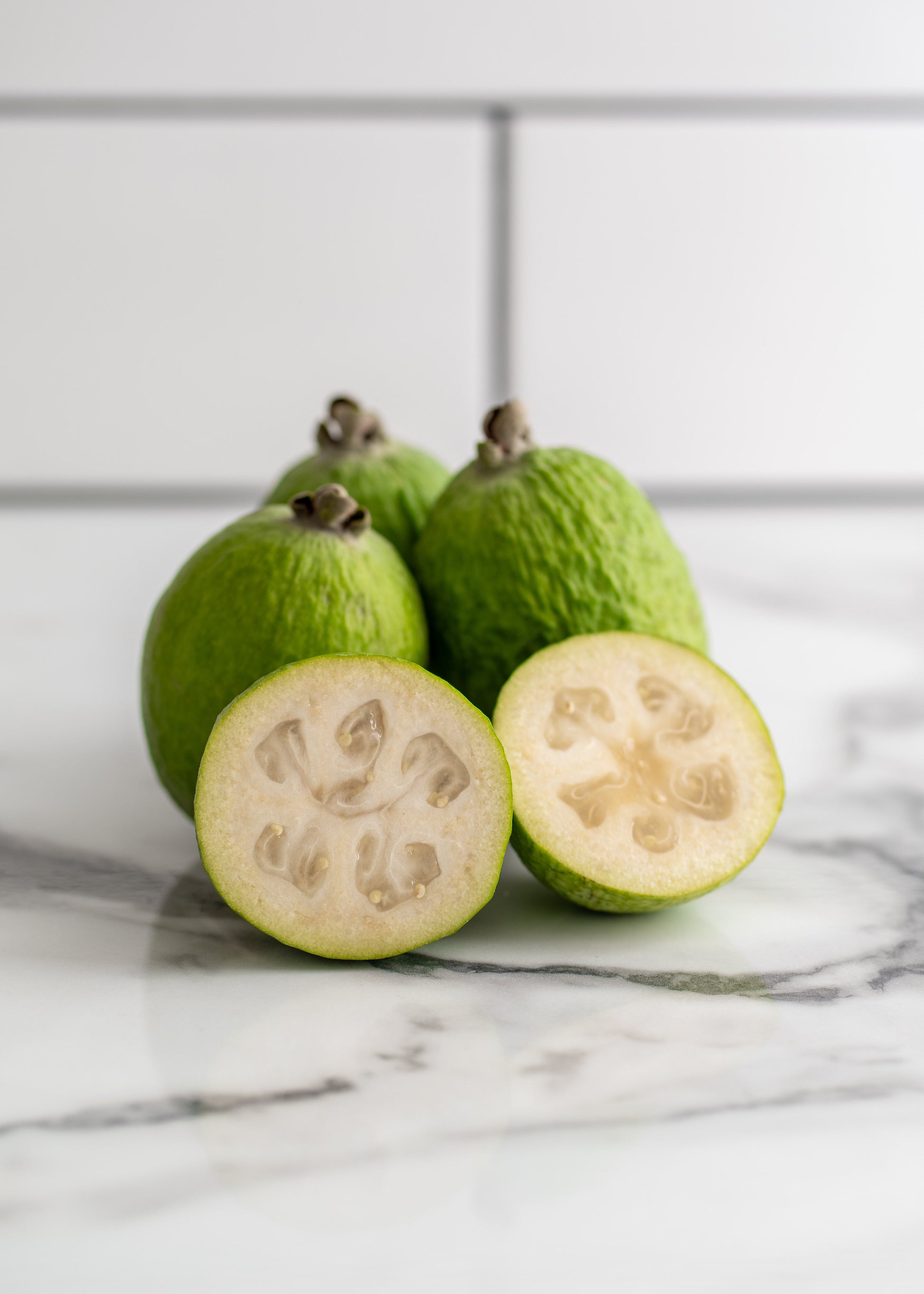 Feijoa fruit with a sliced feijoa on a marble surface