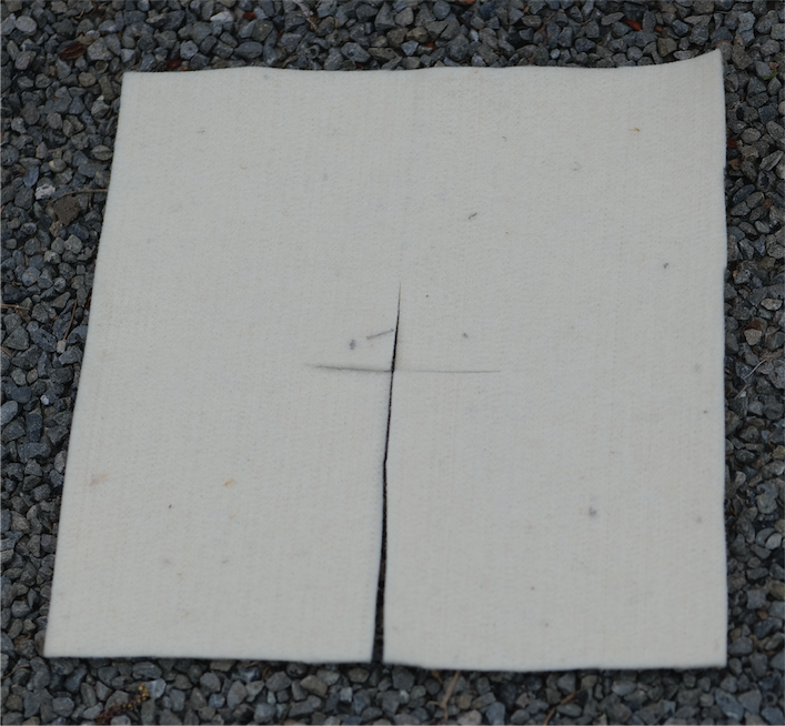 A square of felted wool with a vertical slit down the center, laid flat on a bed of gray gravel.