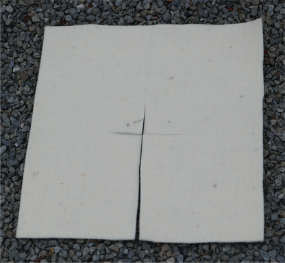 A square of felted wool with a vertical slit down the center, laid flat on a bed of gray gravel.